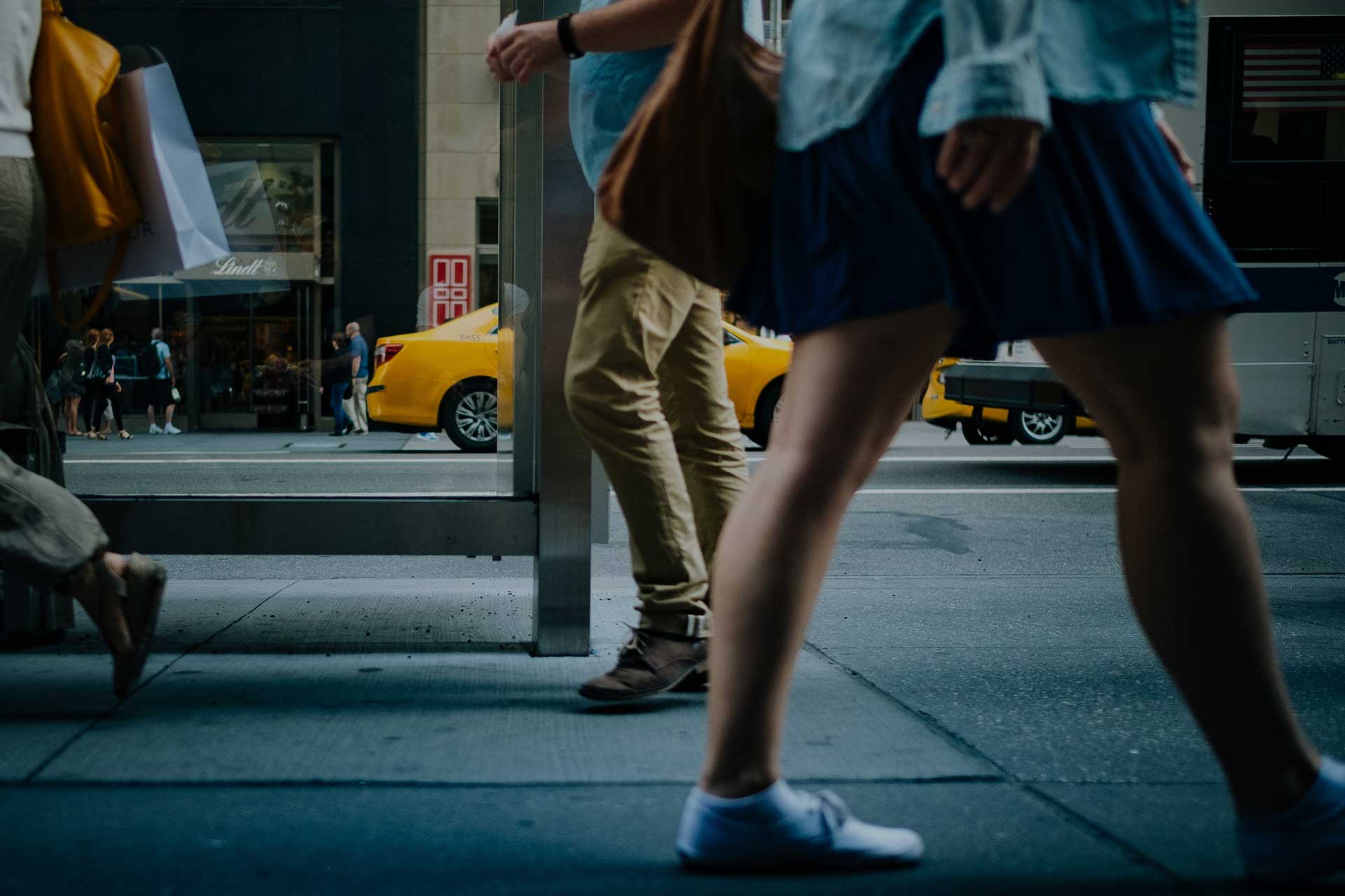 People walking on a city sidewalk near a yellow taxi.